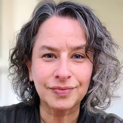 Headshot of smiling, curly-haired woman in olive green shirt