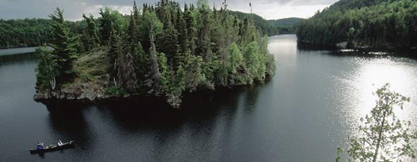 Wide shot of tree covered island. Canoe floating in left foreground