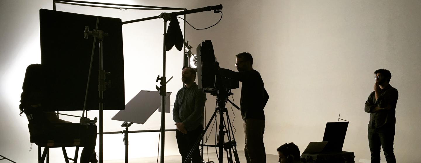 Shadowy film crew with equipment against a white background